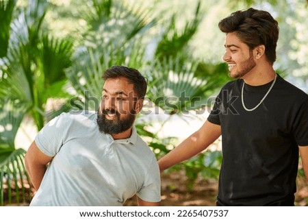 Two funny indian men laughing and speak Hindi in public park green palm leaves background, true male friendship. Two amusing indian guys laughing out loud on outdoor walking in park