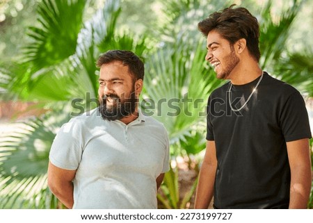 Two funny indian men laughing and speak Hindi in public park green palm leaves background, true male friendship. Two amusing indian guys laughing out loud on outdoor walking in park
