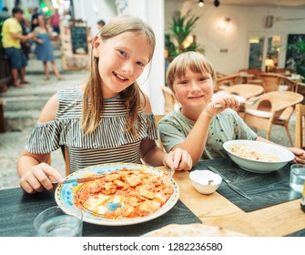 Two Funny Kids Having Lunch In The Restaurant, Eating Ravioli And Pasta