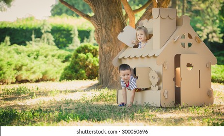 Two funny kids are playing in a cardboard toy house. In a summer day in the park