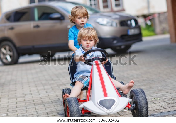Two funny\
little boy friends having fun with toy race car in summer garden,\
outdoors. Active kid pushing the car with younger boy. Outdoor\
games for children in summer\
concept.