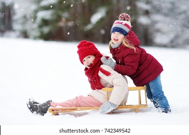 Two Funny Little Girls Having Fun With A Sleight In Beautiful Winter Park. Cute Children Playing In A Snow. Winter Activities For Kids.