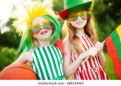 Two funny little sisters supporting and cheering their national basketball team during basketball championship. Two cute Lithuanian team fans.
