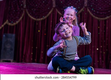 Two funny playful children, boy and girl, smiling while acting as monsters with claws, on a purple stage, in a theatrical representation
