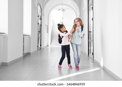 Two funny school girls playing and having fun together, running on long corridor. African and Caucasian girl with different in age studying together in International school. Concept of friendship.