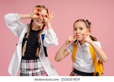 Two funny schoolgirls making grimaces and having fun together on a pink background - Powered by Shutterstock