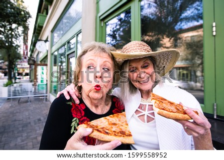 Two funny senior women eating street food pizza