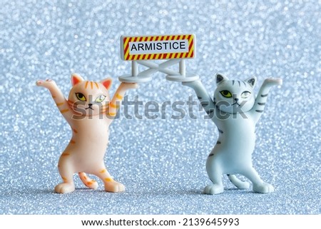 Two funny toy kittens are holding a sign that says armistice. Silver background. Close-up