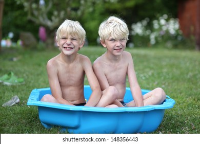 Two Funny Twin Brothers Sitting In A Small Plastic Kiddie Pool At The Backyard Of The House