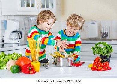 Two Funny Twin Kids Cooking Italian Meal With Spaghetti And Fresh Vegetables In Home's Kitchen. Sibling Children In Colorful Shirts.