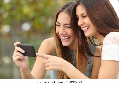 Two Funny Women Friends Laughing And Sharing Social Media Videos In A Smart Phone Outdoors