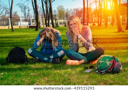 Two funny women sitting on the grass in the park relaxing