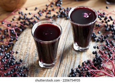 Two galsses of homemade black elder syrup with fresh elderberries on a wooden table
