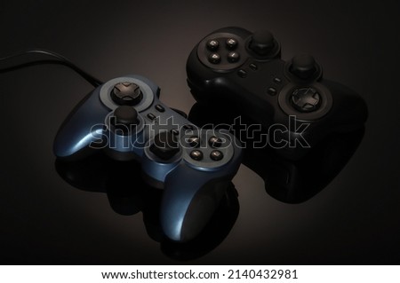 Two game joysticks, gamepads, black and blue on a black gradient background, opposite each other