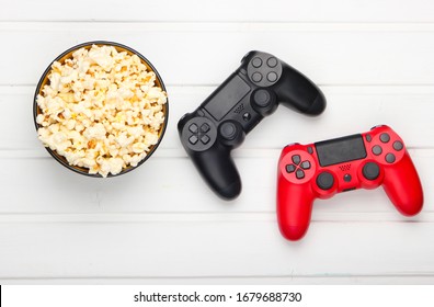 Two gamepads and a bowl of popcorn on white wooden table. Gaming, leisure and entertainment concept. Top view - Powered by Shutterstock