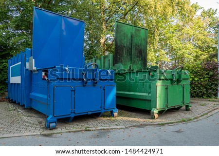 two garbage compactors Standing next to each other on the premises of a hospital