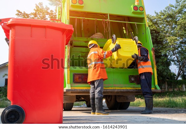 Two garbage men\
working together on emptying dustbins for trash removal with truck\
loading waste and trash\
bin.