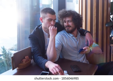 Two gay male friends hugging in a cafe, smiling and having a cigarette. LGBT and love concept. - Shutterstock ID 1856046985