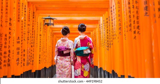 Two geishas among red wooden Tori Gate at Fushimi Inari Shrine in Kyoto, Japan. Selective focus on women wearing traditional japanese kimono.