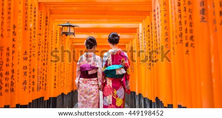 Two geishas among red wooden Tori Gate at Fushimi Inari Shrine in Kyoto, Japan. Selective focus on women wearing traditional japanese kimono.