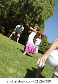 Two Generation Family Playing Softball In Park, Girl (6-8) Batting, Smiling (tilt)