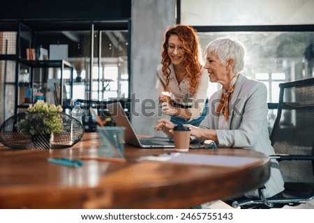 Two generation workers collaborating on a innovative project on a laptop at the modern office.Senior female manager typing on a laptop while her young colleague helping her with creating business plan