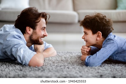 Two Generations. Profile Portrait Of Happy Father And His Son Lying On Carpet At Home, Looking At Each Other And Smiling. Family Spending Time Together At Home, Side View