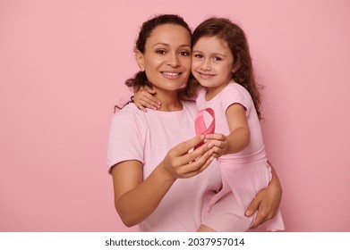 Two generations of women, lady and girl, mother and daughter posing against a pink background, holding a pink ribbon, showing support and solidarity to patients and cancer survivors. Medical awareness - Shutterstock ID 2037957014