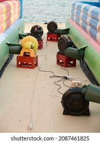 Two Giant Color Fabric Trampoline Castles Laying Down On Ground Inflating With Electric Air Blowers On Plastic Boxes Side View