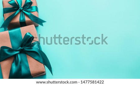Two gift boxes in craft wrapping paper and green satin ribbon on turquoise blue background, copy space right. Beautiful Christmas, New Year or Birthday presents, flat lay or top view. Banner