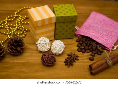 Two gift boxes - yellow and green, fir cones, balls of vine and coffee beans in a pink pouch on a wooden table - Powered by Shutterstock