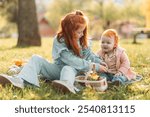 Two ginger, redhead little girls sitting outdoors in the park, playing