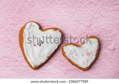 Two gingerbread cookies with white icing are on a pink background.