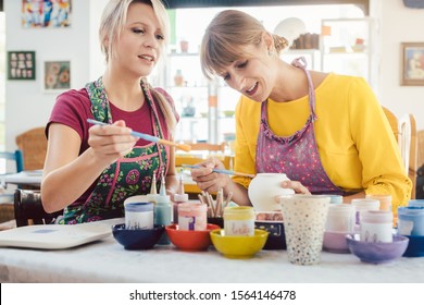 Two Girl Friends Painting Their Own Handmade Ceramics In A Hobby Workshop