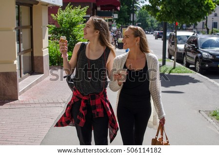 Two girlfriends are eating icecream and drinking coffee on the stret