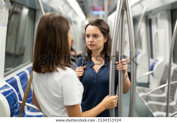 Two girlfriends enjoying friendly\
conversation while traveling on subway\
train\
\
