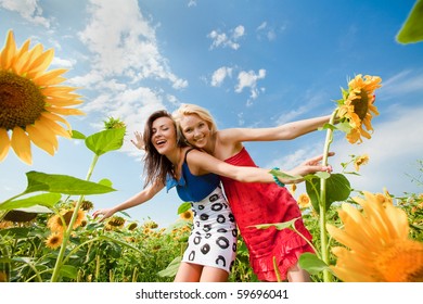 Two Girlfriends Having Fun In Field Of Sunflowers