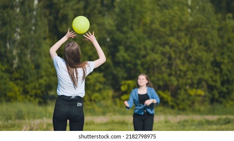 Two girlfriends play volleyball in the meadow.