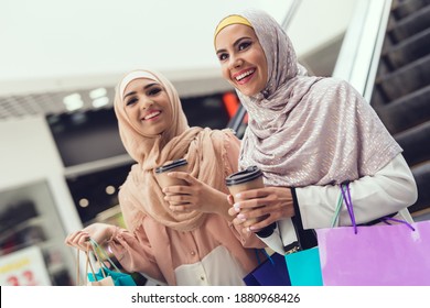 Two girlfriends smile while drinking coffee in the mall. Two women with packages in hand are walking in the mall.  - Powered by Shutterstock