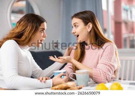 Two girlfriends talking and drinking tea together, spending day together at home