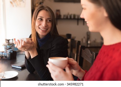 Two Girlfriends Talking Over Coffee In Cafe