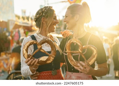 Two girlfriends together holding pretzel or brezen on a Bavarian fair or oktoberfest or duld in national costume or Dirndl in germany 