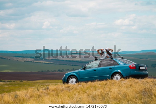 Two girlfriends travel by car in the mountains in\
the summer, women look forward from the hatch of the car with their\
backs to the frame.