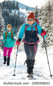 two girls with backpacks walk through the snow among the trees. winter hiking in the mountains. adventure in the mountains. - Shutterstock ID 2200358651