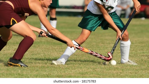Two girls battle for control of the ball in a field hockey game