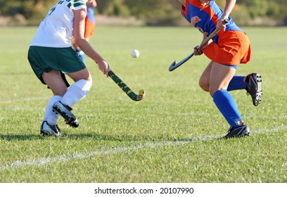 Two girls battle for control of the ball in a field hockey game