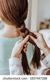 Two girls braid their hair at the window. Woman makes a braid to her friend. Hair weaving hairstyles. Girlfriend braids her hands with ringlets. Hair care