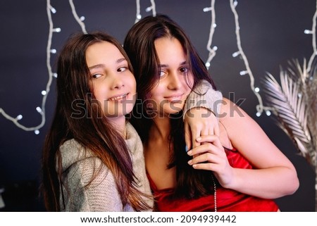 Two girls brunette friends making fun embracing smiling holding hands over grey background and illumination.