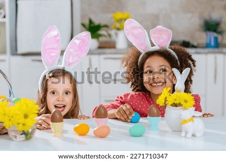 Two girls with Bunny ears on her heads is happy find a chokolate eggs after Easter egg hunt.