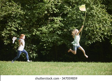 Two Girls Chasing Butterflies In Summer Field